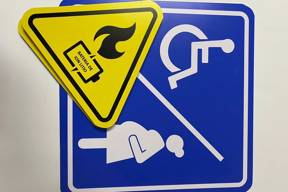 Señalamientos rígidos recién impresos: placa azul de accesibilidad y triángulo amarillo de advertencia