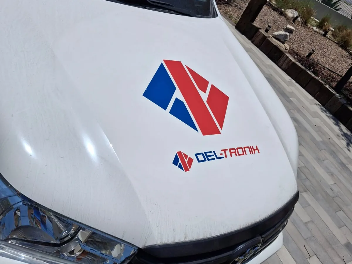 Logotipo en vinil azul y rojo aplicado sobre el cofre de una camioneta blanca, visto de cerca