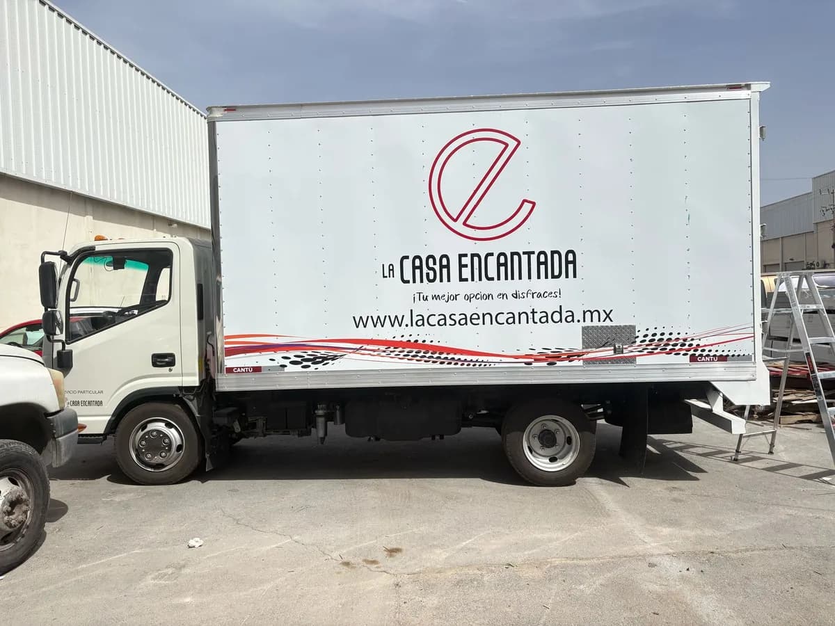 Camión de caja seca con logotipo, nombre comercial y sitio web en vinil sobre el costado, estacionado en un patio