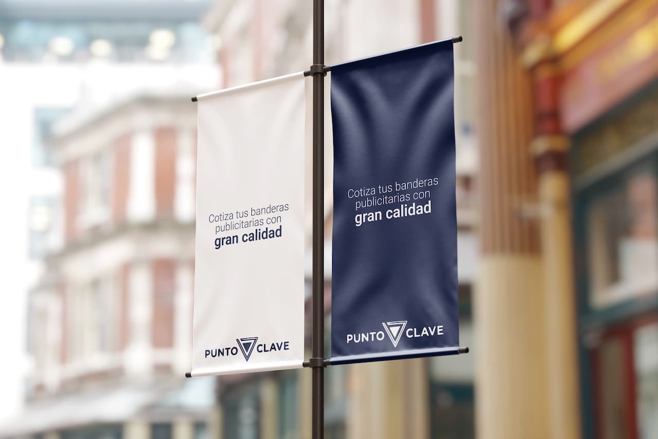 Se observan dos banderas publicitarias colgadas en un soporte. Una es blanca y la otra es azul, ambas presentan el texto 'Cotiza tus banderas publicitarias con gran calidad' y el logo de 'punto clave', ofreciendo un mensaje claro y atractivo para sus servicios.