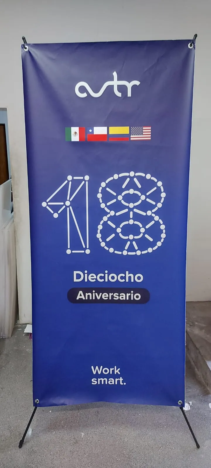 Banner tipo araña con estructura en X y gráfico azul de aniversario número dieciocho, armado en el taller