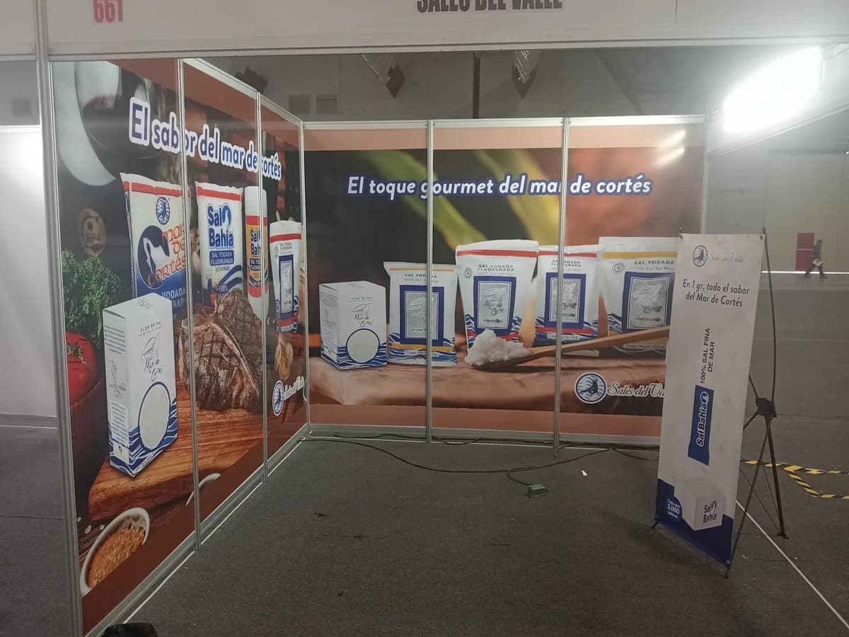 Stand de exposición con paredes gráficas impresas de productos alimenticios y un banner tipo araña, armado en el pasillo de una feria
