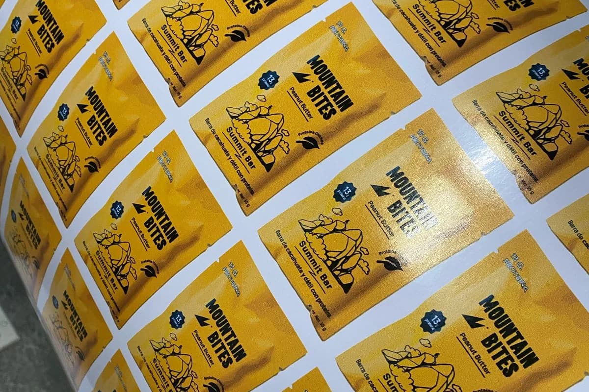 Planilla de etiquetas amarillas de vinil con ilustración de montaña, recién impresas y troqueladas a forma en el taller