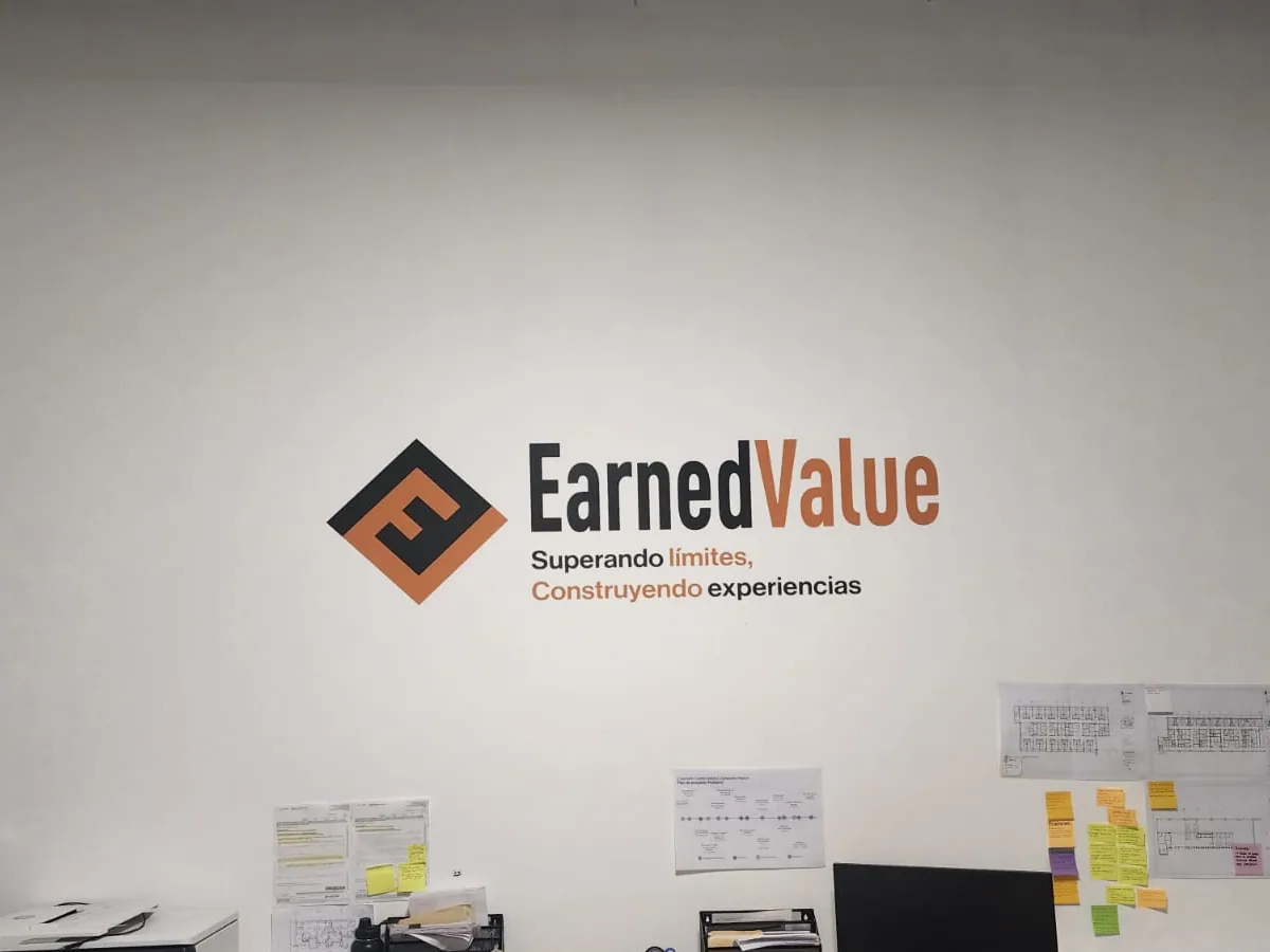 Logotipo y eslogan de empresa en vinil de corte naranja y negro aplicados sobre el muro blanco de una oficina