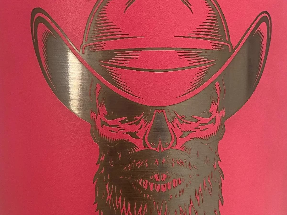 Ilustración de una calavera con sombrero y barba grabada con láser sobre un termo rosa, vista de cerca