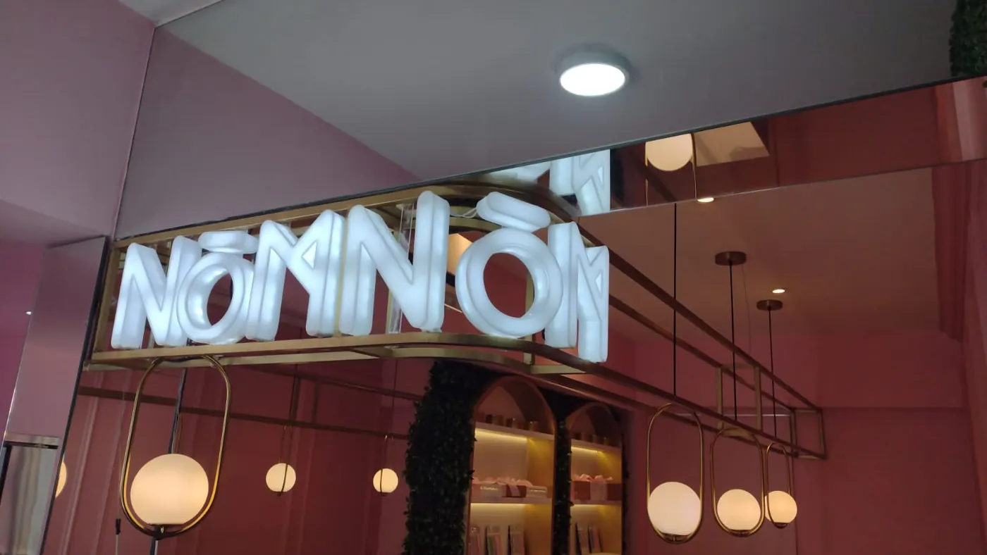 Letras luminosas blancas de un restaurante montadas en una estructura dorada sobre pared rosa
