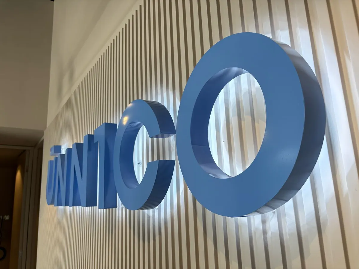 Letras 3D azules con iluminación trasera que proyecta un halo blanco sobre un muro de listones