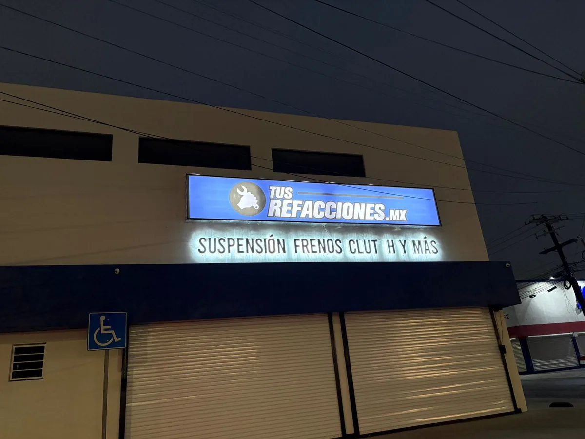 Anuncio luminoso con el nombre del negocio sobre la cortina de un local, encendido de noche