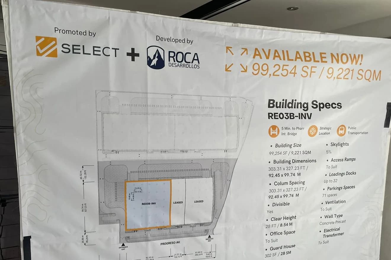 Lona blanca con el plano y las especificaciones de una nave industrial, tensada en un bastidor dentro de una oficina