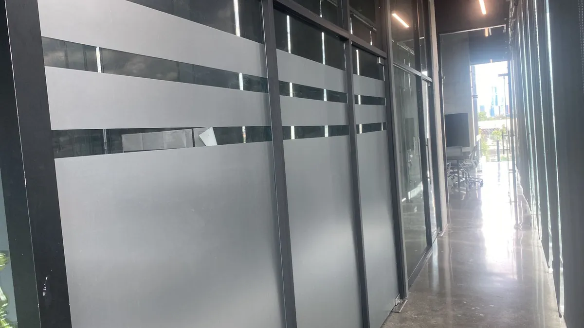 Pasillo de oficinas con canceles de vidrio cubiertos de vinil esmerilado en franjas para dar privacidad sin perder luz